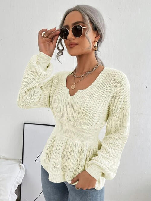 Woman wearing a chic notched dropped shoulder knit top in 100% acrylic. Available in sizes S to XL, offering a slightly stretchy and comfortable fit. Easy care with machine wash cold and tumble dry low. 