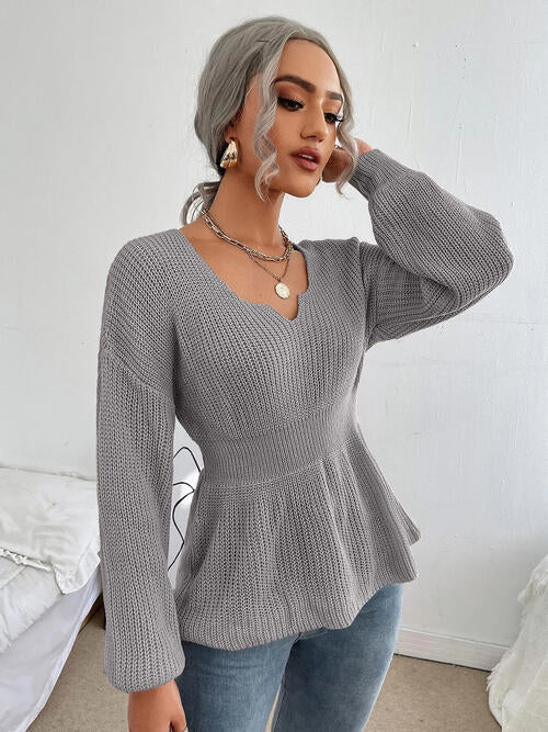 Woman wearing a chic notched dropped shoulder knit top in 100% acrylic. Available in sizes S to XL, offering a slightly stretchy and comfortable fit. Easy care with machine wash cold and tumble dry low. 