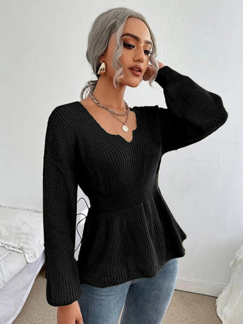 Woman wearing a chic notched dropped shoulder knit top in 100% acrylic. Available in sizes S to XL, offering a slightly stretchy and comfortable fit. Easy care with machine wash cold and tumble dry low. 