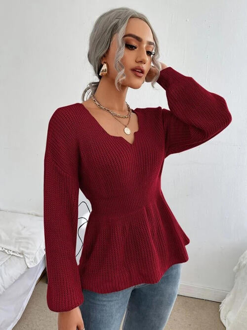 Woman wearing a chic notched dropped shoulder knit top in 100% acrylic. Available in sizes S to XL, offering a slightly stretchy and comfortable fit. Easy care with machine wash cold and tumble dry low. 