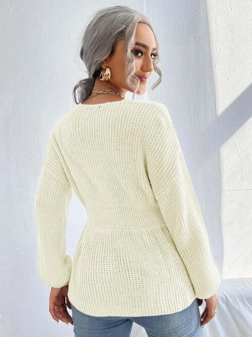 Woman wearing a chic notched dropped shoulder knit top in 100% acrylic. Available in sizes S to XL, offering a slightly stretchy and comfortable fit. Easy care with machine wash cold and tumble dry low. 