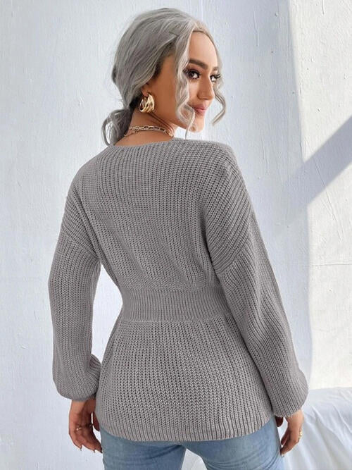 Woman wearing a chic notched dropped shoulder knit top in 100% acrylic. Available in sizes S to XL, offering a slightly stretchy and comfortable fit. Easy care with machine wash cold and tumble dry low. 